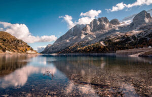serene alpine lake reflecting jagged snow dusted mountains under a blue sky with a few clouds