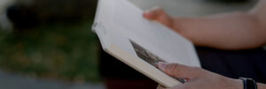 person reading an open book outdoors hands visible on the pages