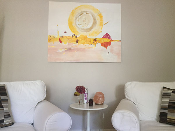 Ruhige Sitzsituation mit zwei weißen Sesseln, kleinem Tisch und abstraktem Kunstbild in warmen Farben.